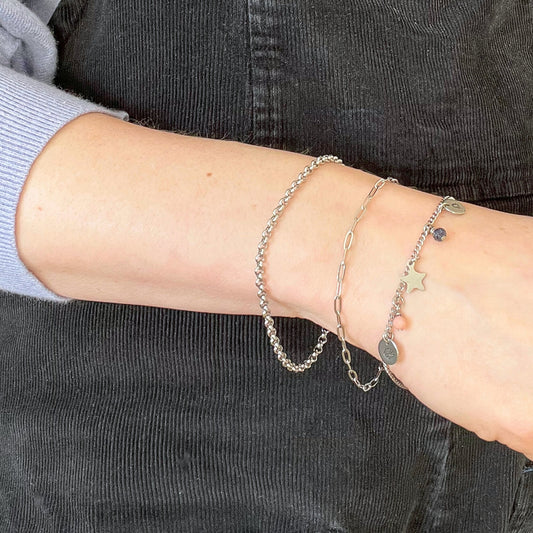 Pale woman wearing three chain bracelets one of which has small charms dangling from it.