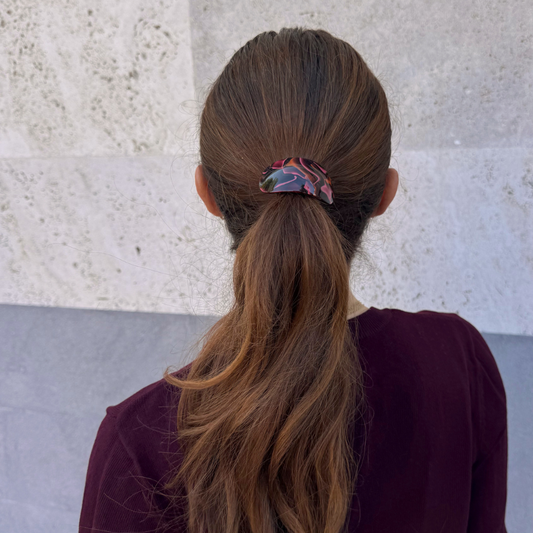 Person with long brown hair in a ponytail wearing a maroon sweater against a light stone wall.