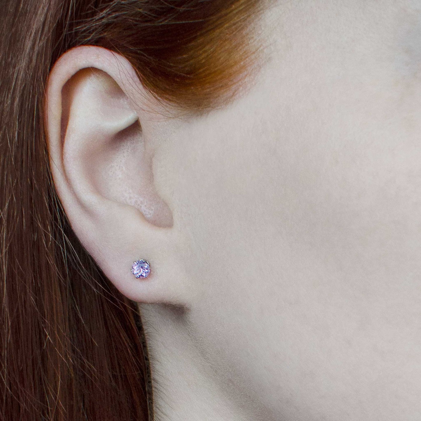 Woman wearing tiny purple Amethyst stud earrings in earlobe