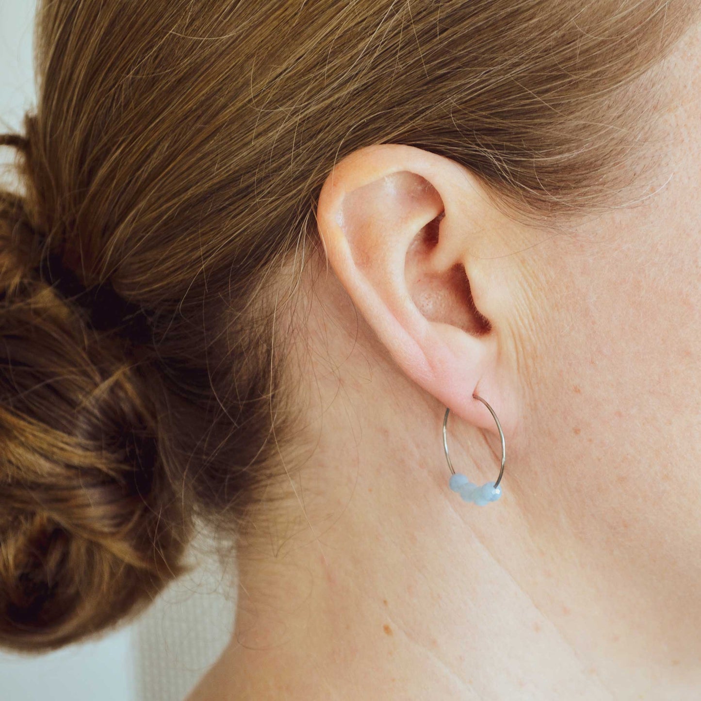 Woman wearing pale blue Aquamarine hoop earring in earlobe