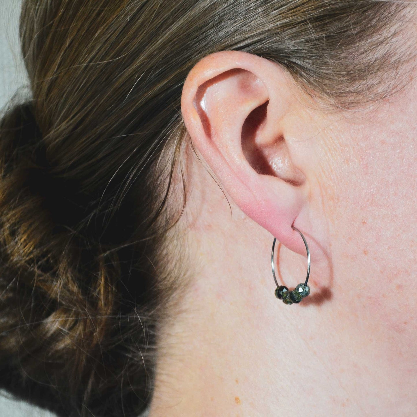 Woman wearing dark green hoop earrings in earlobe