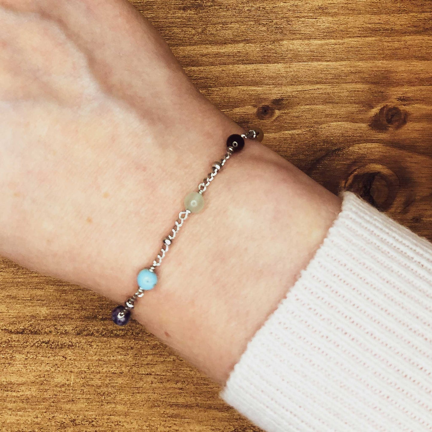 Woman wearing pink jumper and dainty chakra bracelet on wrist