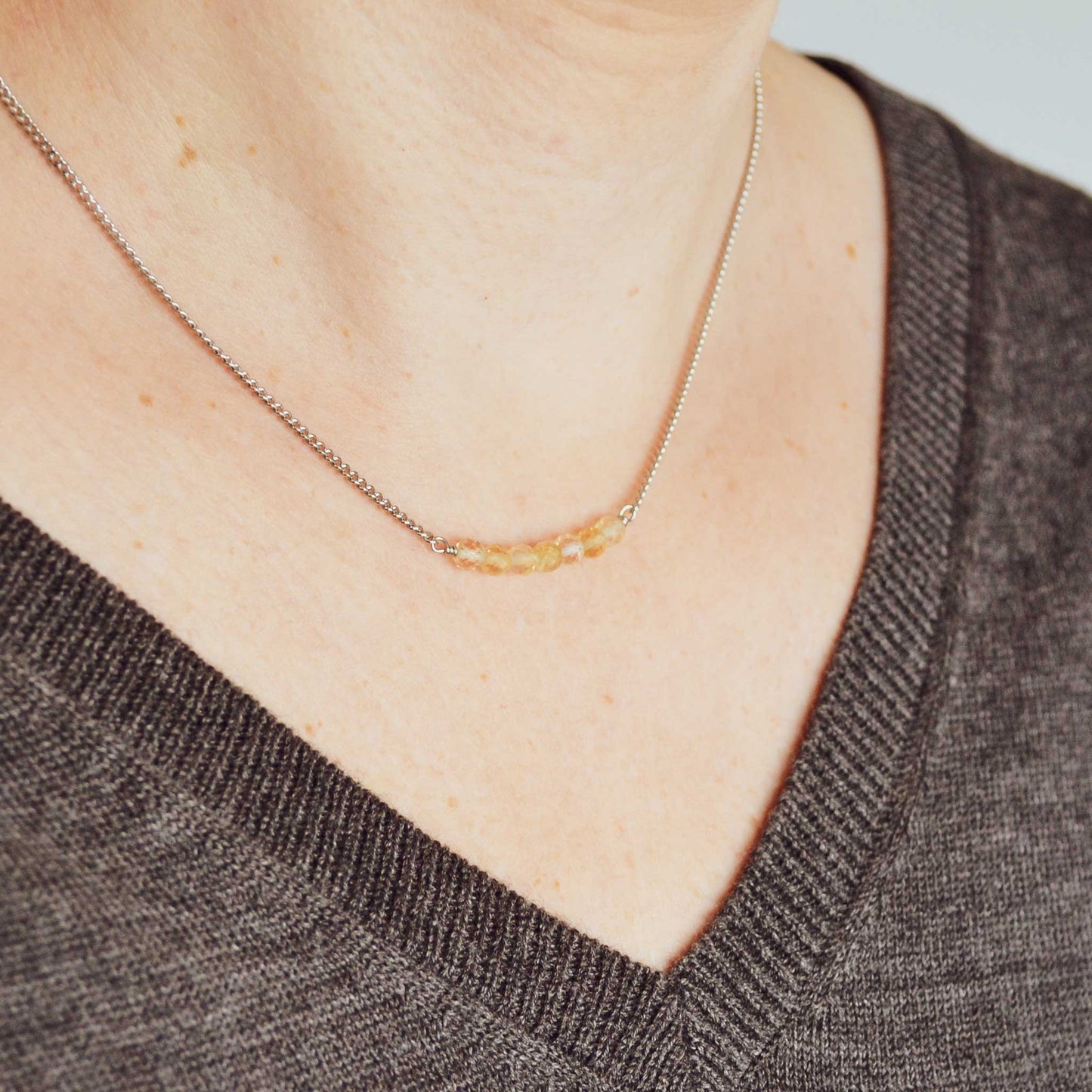 Woman wearing grey v neck jumper and dainty yellow Citrine crystal necklace