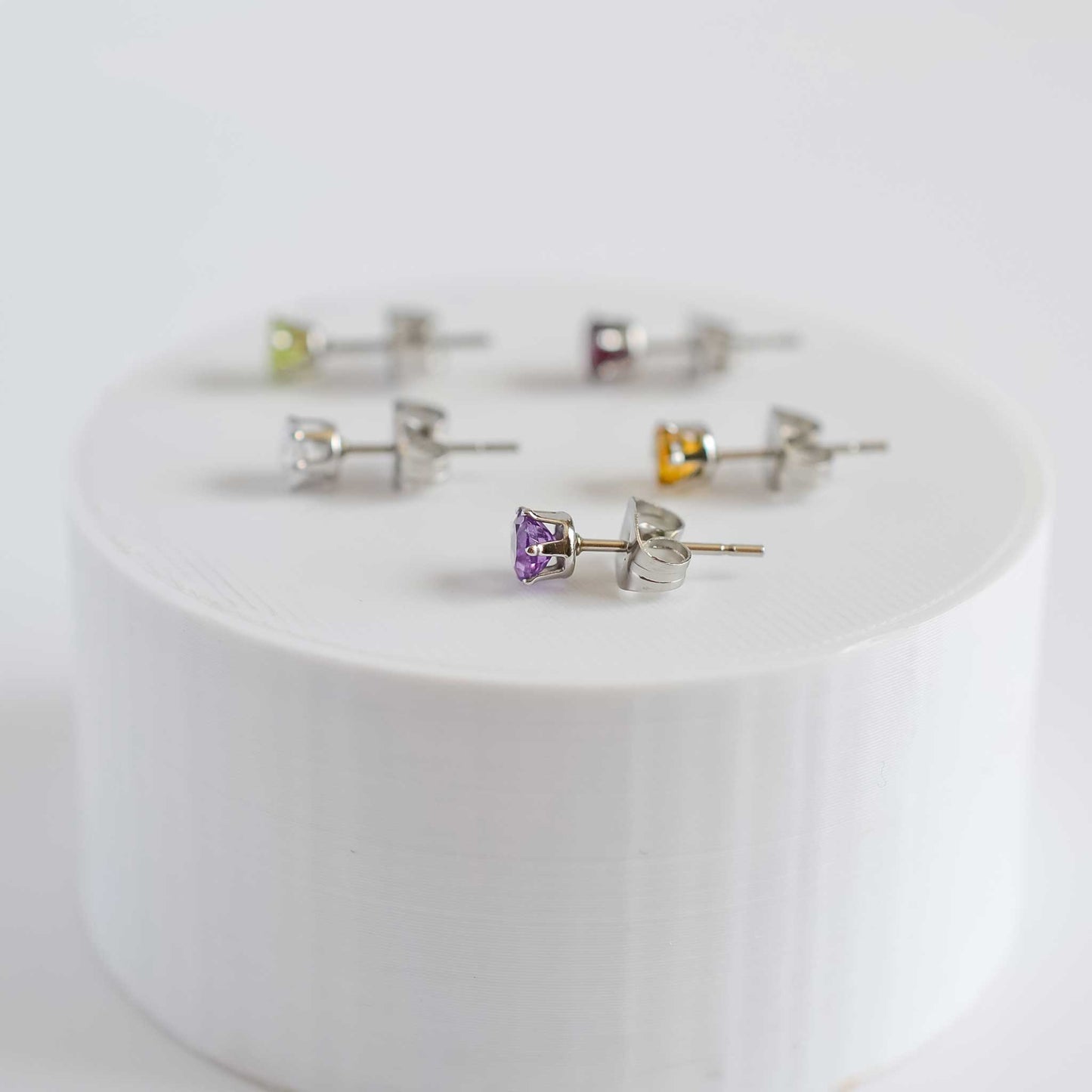 Side view of five small gemstone stud earrings on round white plinth