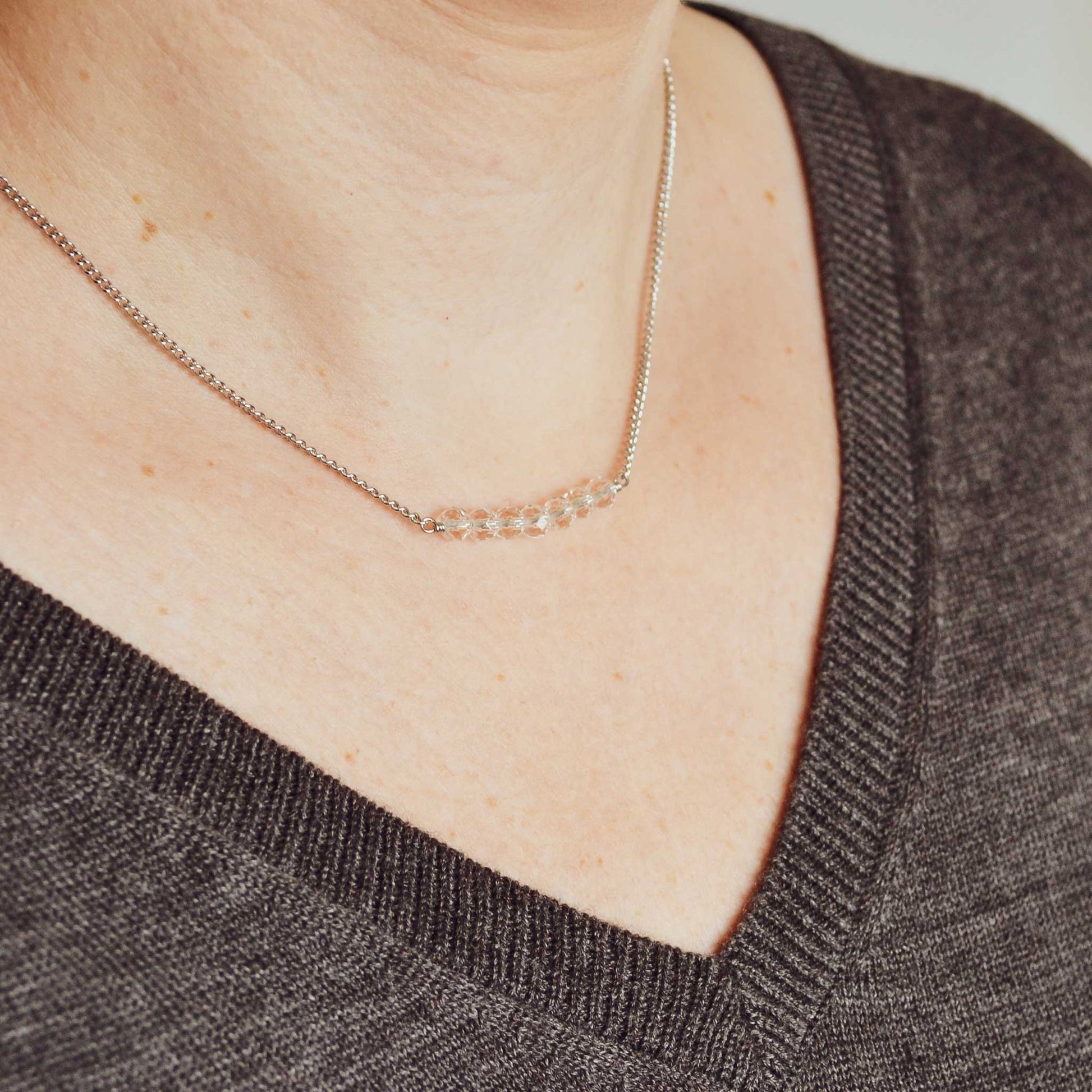Woman wearing grey v neck jumper and dainty clear crystal necklace