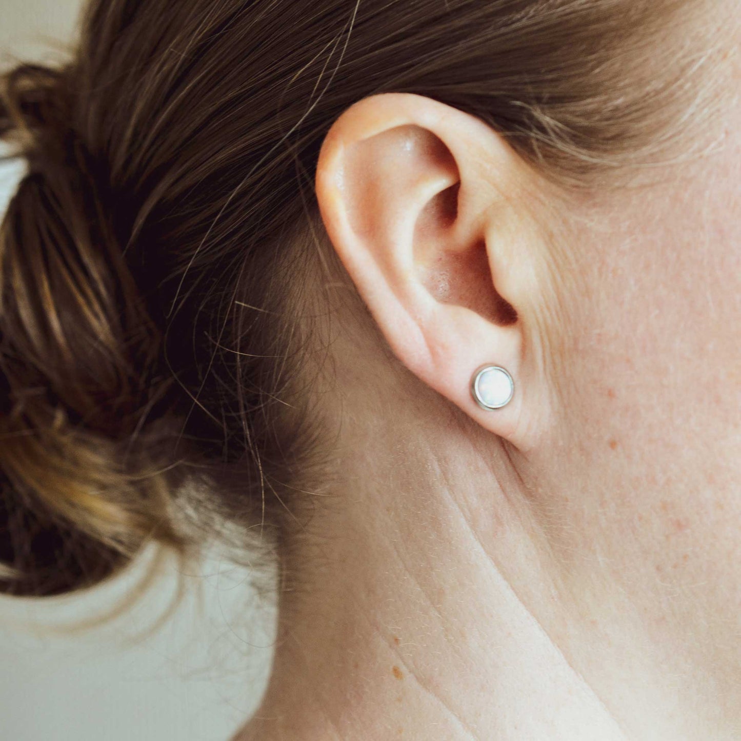 Woman wearing hypoallergenic round white Opal earring in earlobe