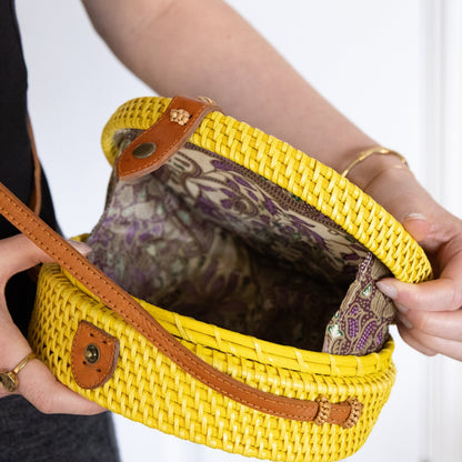 Yellow woven handbag with brown accents held by a person against a white background