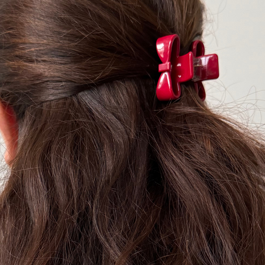 Close-up of red hair clips in a person's wavy brown hair against a neutral background
