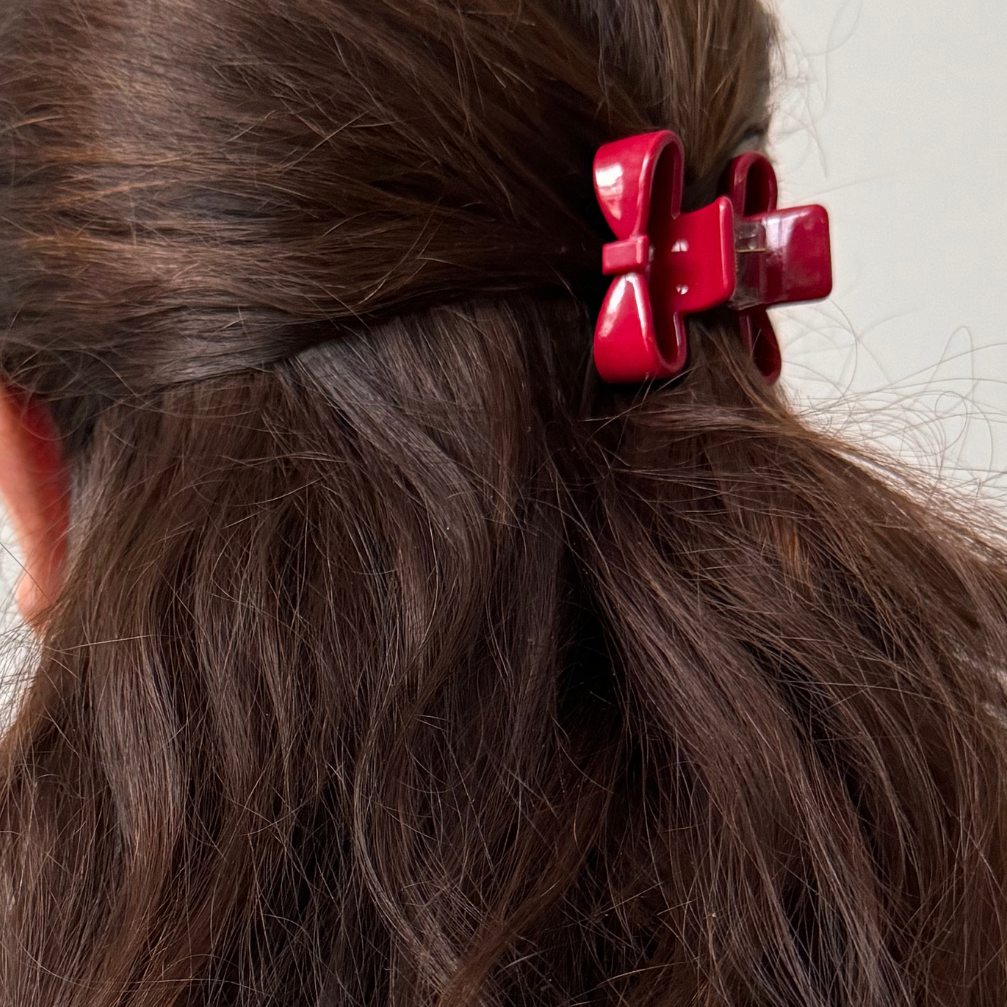 Close-up of red hair clips in a person's wavy brown hair against a neutral background