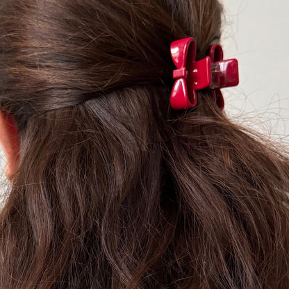 Close-up of red hair clips in a person's wavy brown hair against a neutral background
