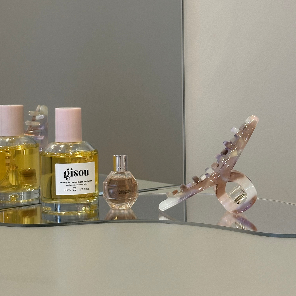 Perfume bottles and hair clip on a reflective surface with a neutral background