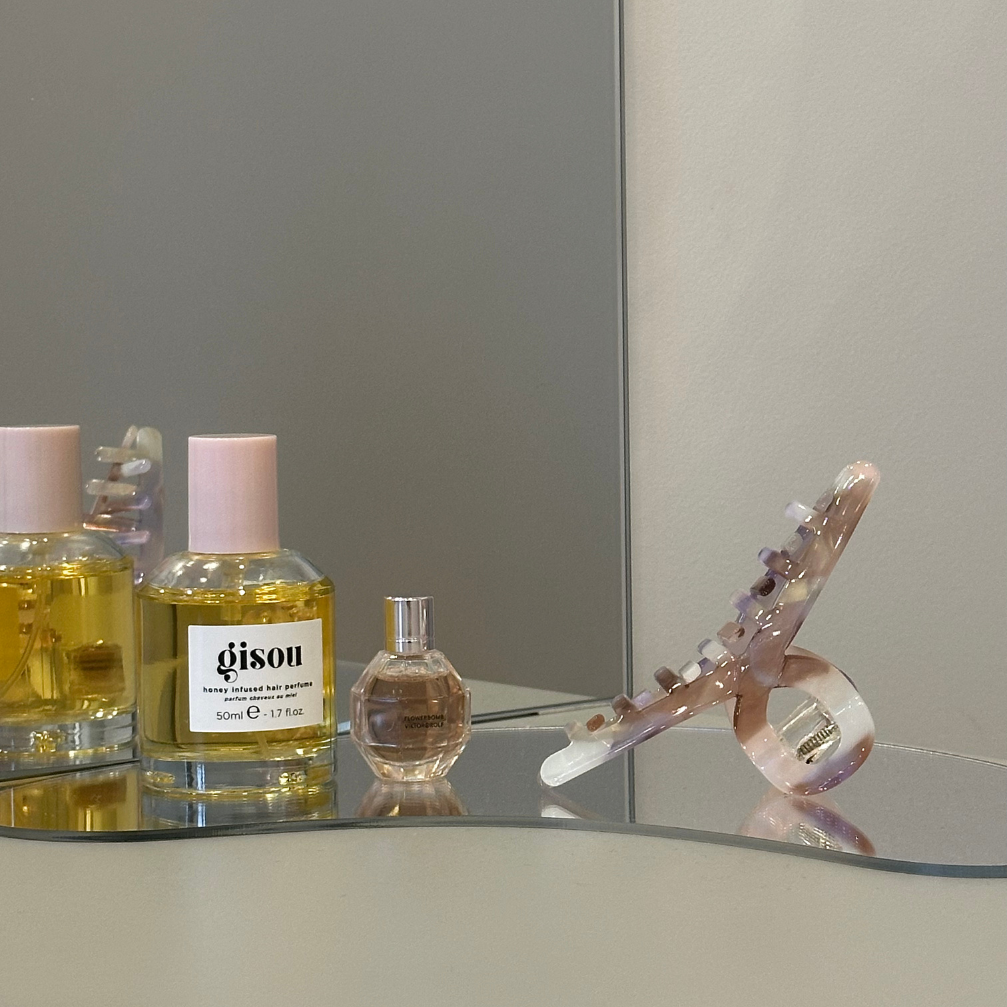 Perfume bottles and hairclip on a reflective surface with a neutral background
