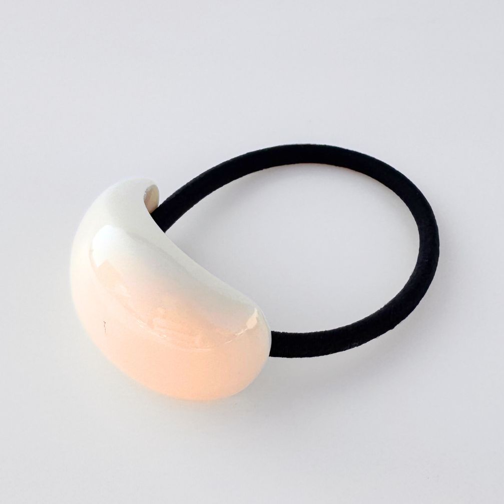 Hair tie with a cream ceramic ball on a light gray background