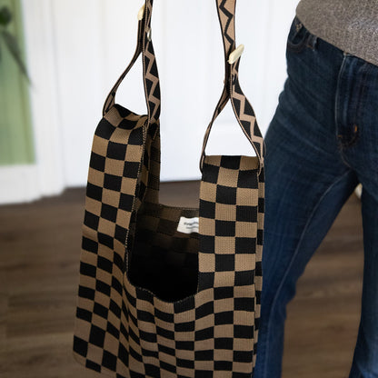 Black and beige checkered bag with zigzag strap held by a person wearing blue jeans.
