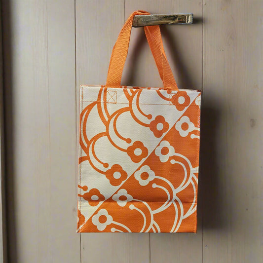 Orange and white patterned tote bag with orange handle hanging on a wooden surface.