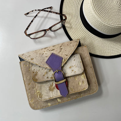 Beige handbag with purple strap, straw hat, and glasses on a light gray background