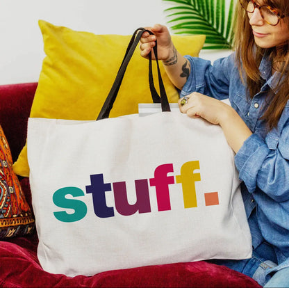Person holding a tote bag with 'stuff.' in colorful letters on a couch.