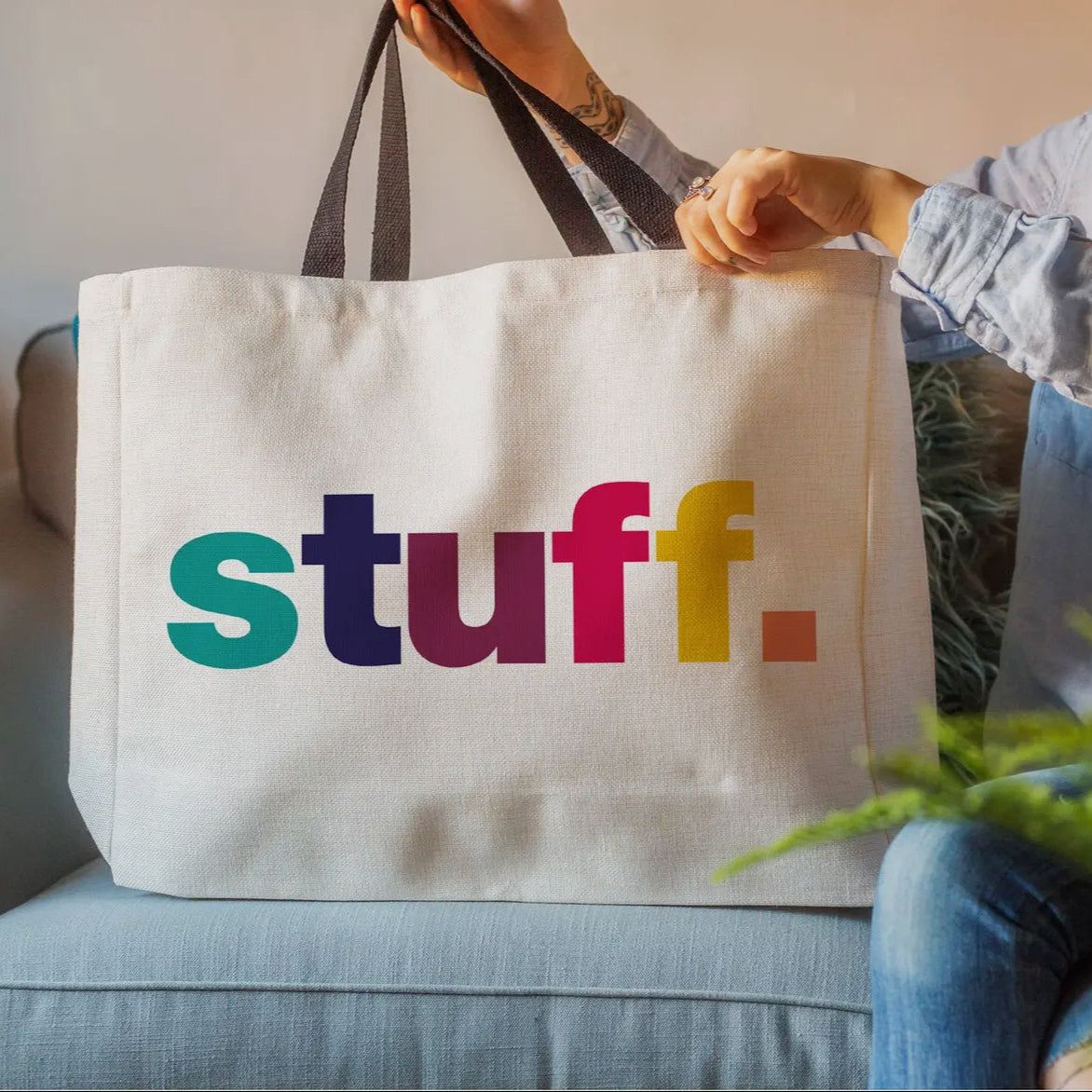 Tote bag with colorful 'stuff.' text held by a person on a couch.