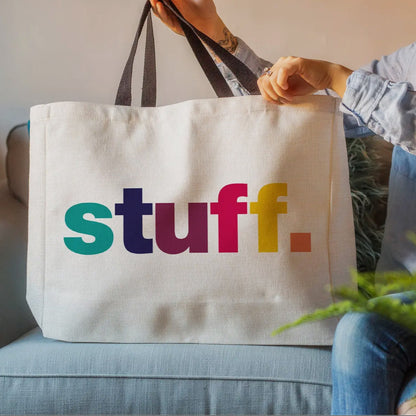 Tote bag with colorful 'stuff.' text held by a person on a couch.