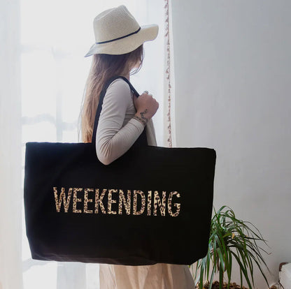 Person holding a black tote bag with 'WEEKNIGHTING' text, wearing a hat indoors.