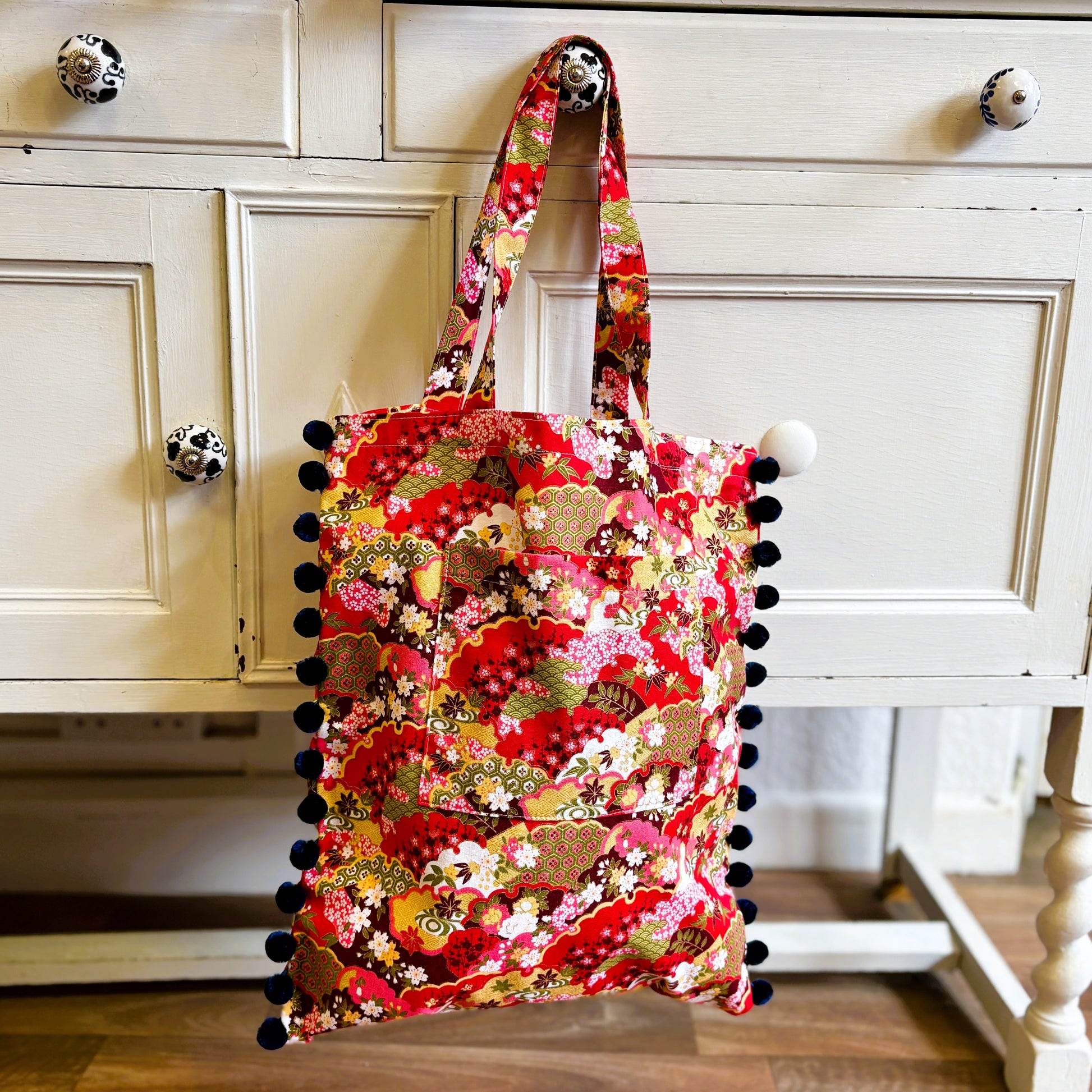 Floral tote bag with pom-pom details on a wooden surface
