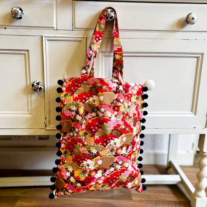 Floral tote bag with pom-pom details on a wooden surface