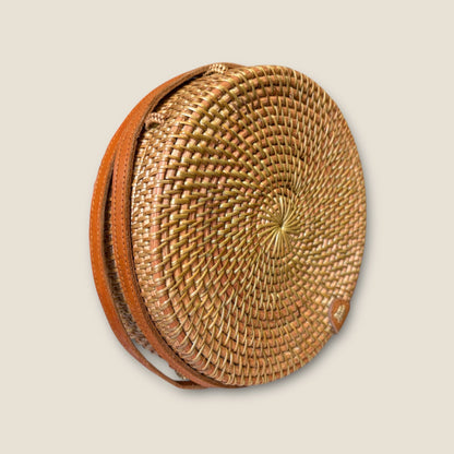 Round woven bag with leather strap on a beige background