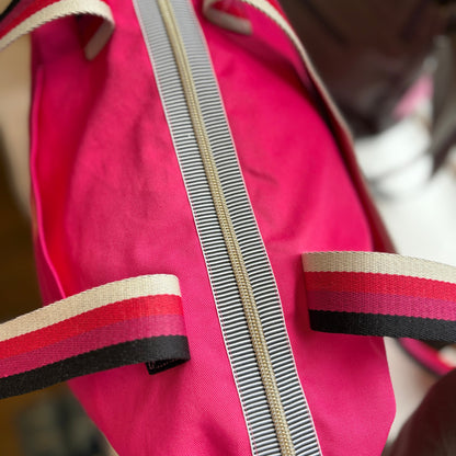 Close-up of a pink bag with striped handles and zipper.