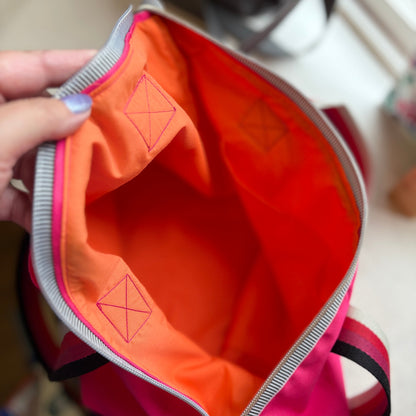 Close-up of a pink and orange bag with a zipper, showing brand logo.