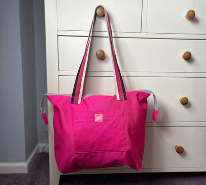 Pink tote bag with a visible brand logo hanging on a white dresser with wooden knobs.