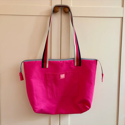 Pink tote bag with black accents hanging on a wooden door.