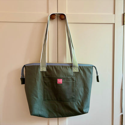 Green tote bag with a red label hanging on a wooden door.