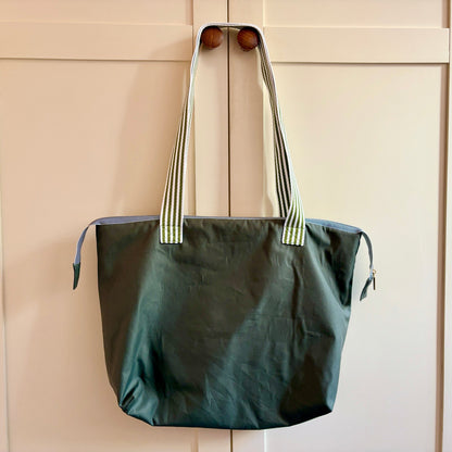 Green tote bag with striped handles on a wooden surface