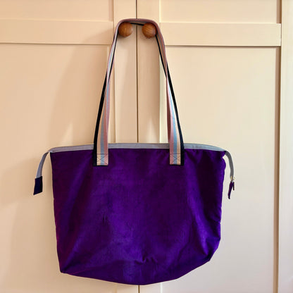 Purple tote bag with striped handles hanging on a wooden door.
