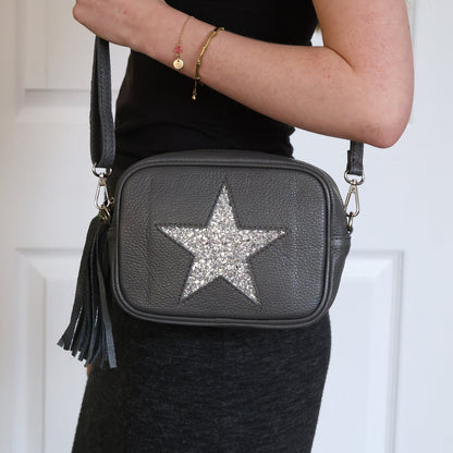 Black handbag with a star design held by a person against a white door background