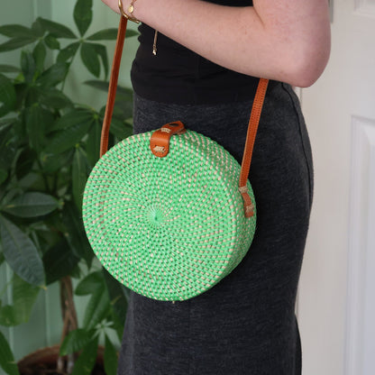 Green woven handbag with brown strap held by a person against a neutral background
