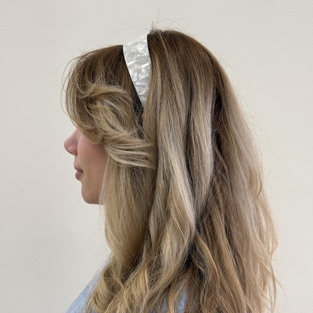Person with long, wavy hair wearing a cream headband against a plain background