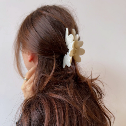 Woman with brown hair wearing a white floral hair clip against a plain background