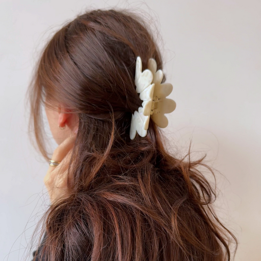 Woman with brown hair wearing a white floral hair clip against a plain background