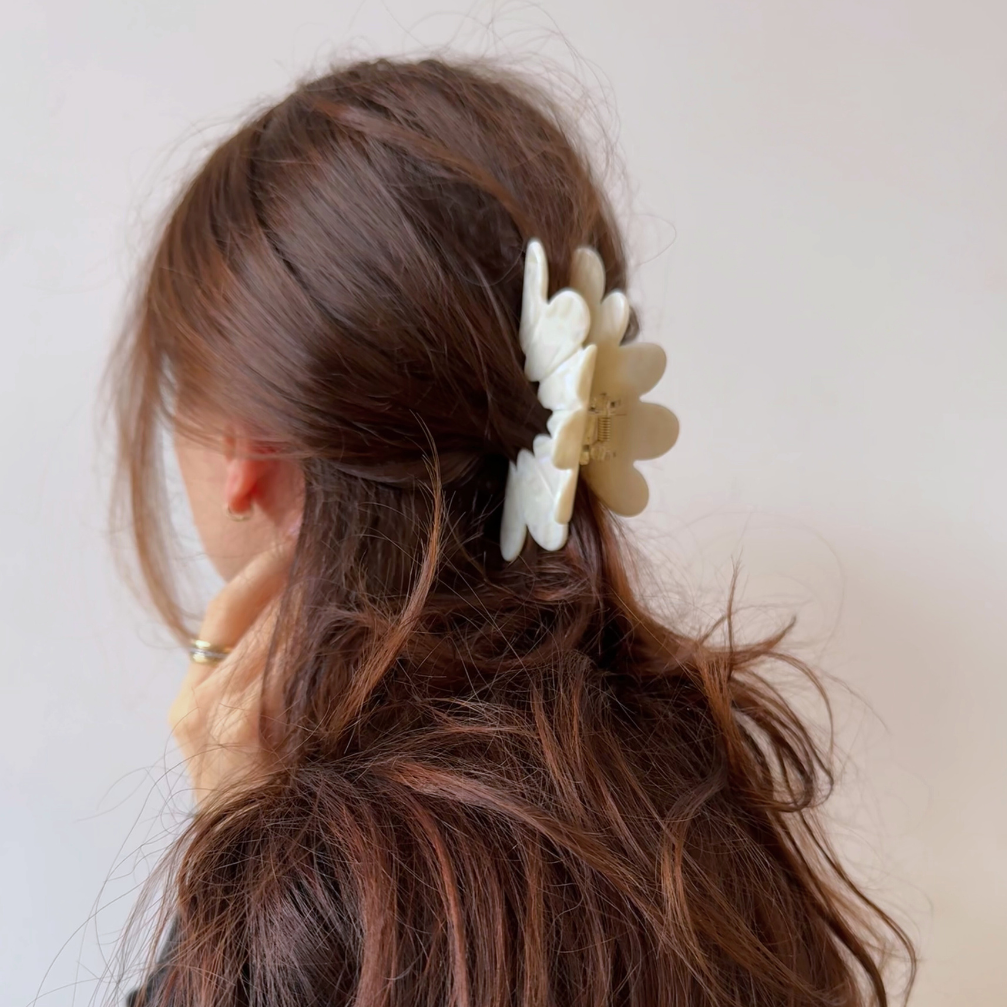 Woman with brown hair wearing a white floral hair clip against a plain background