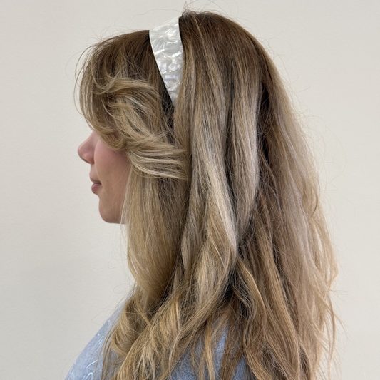 Person with long, wavy hair wearing a cream headband against a plain background
