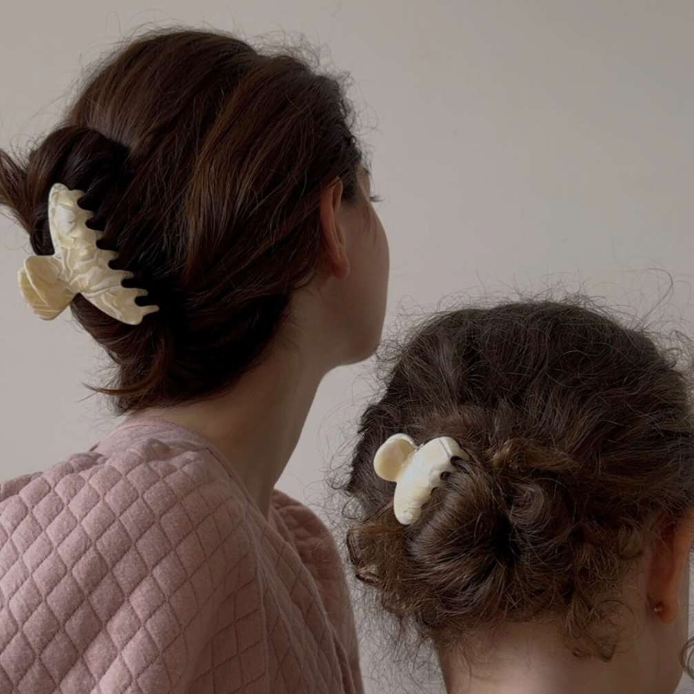 Woman and girl with hair styled using large white hair clips against a plain background