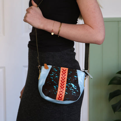 Person holding a crossbody bag with decorative elements against a neutral background