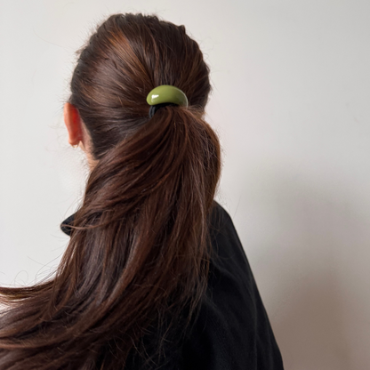 Person with brown hair tied in a ponytail using a green hair tie against a plain background