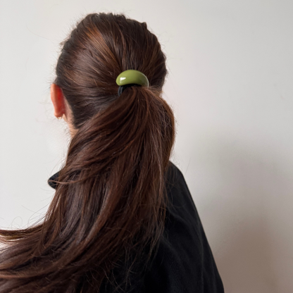 Person with brown hair tied in a ponytail using a green hair tie against a plain background