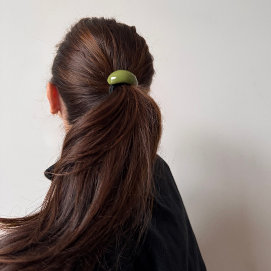 Person with brown hair tied in a ponytail with a green hair tie against a plain background