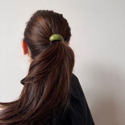 Person with brown hair tied in a ponytail with a green hair tie against a plain background