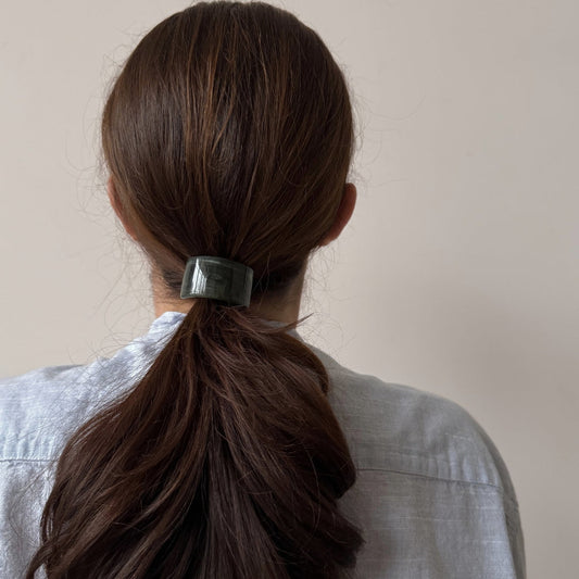 Person with long brown hair tied back with a hair tie against a plain background