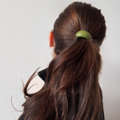 Person with long brown hair tied into a ponytail with a green hair tie against a plain background