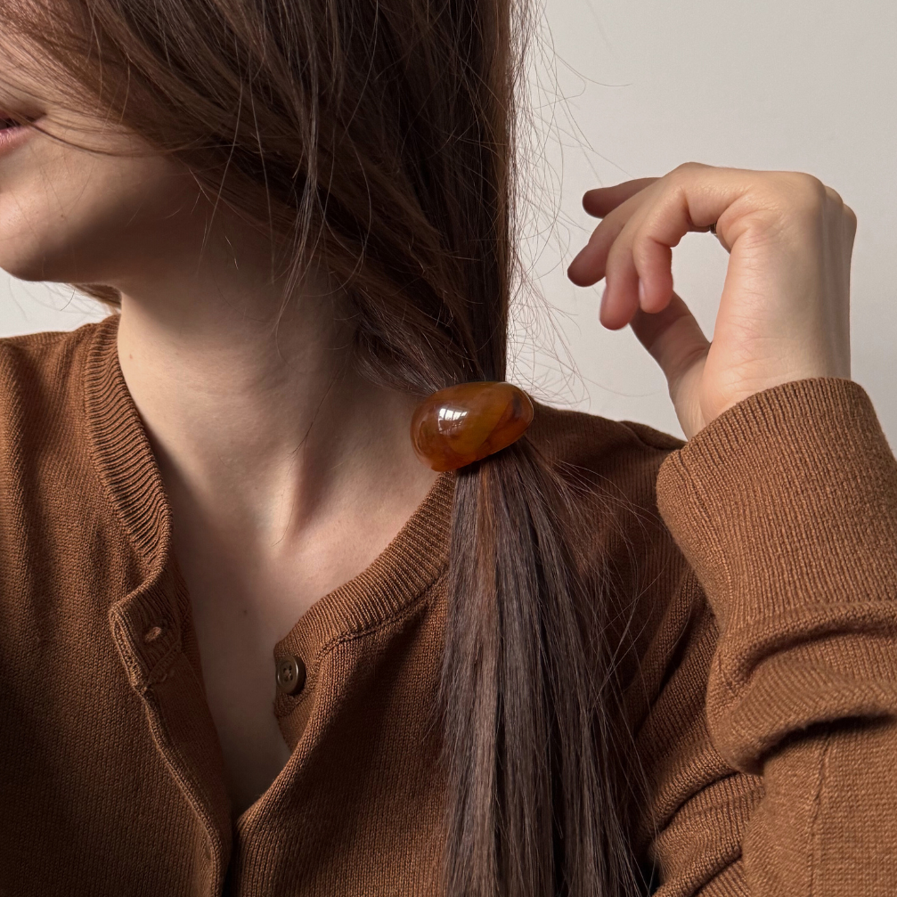 Person wearing a brown cardigan with a hair accessory, against a neutral background